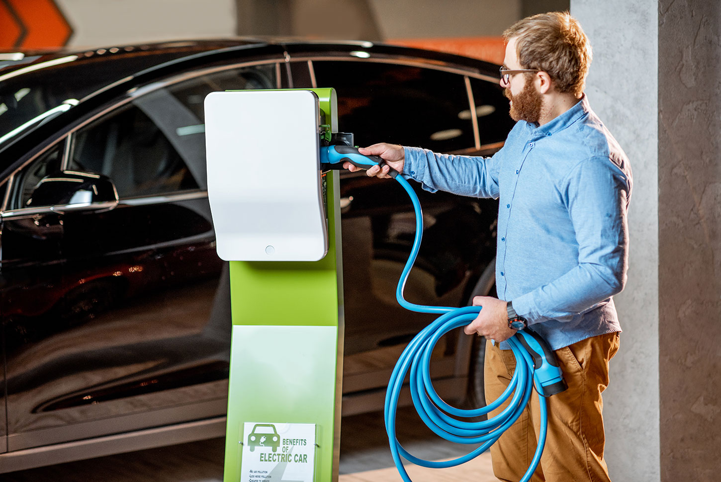 homme qui branche son cable de charge sur une borne de recharge